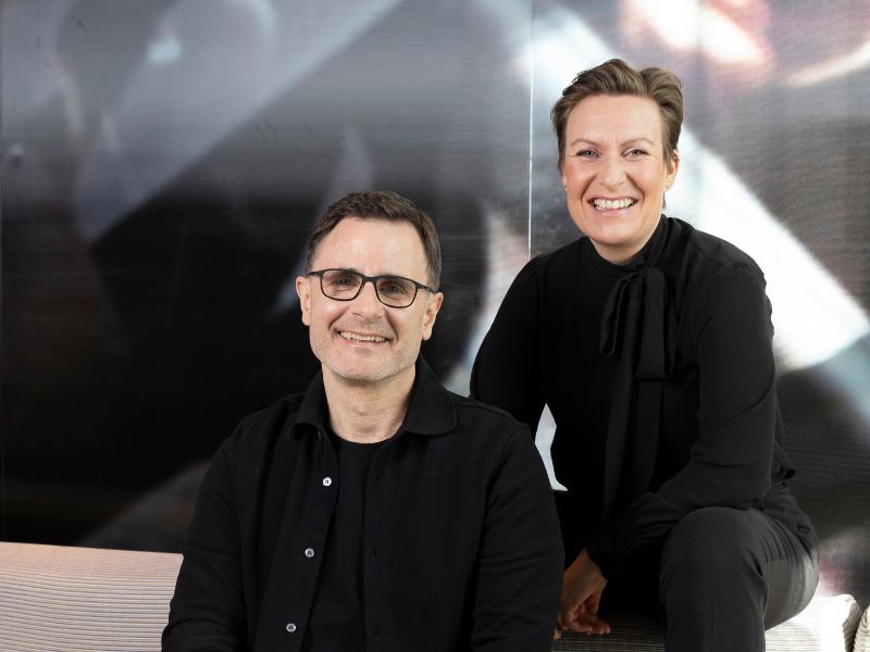 Ein lächelndes Paar sitzt in einem modernen Raum, bereit für ein kreatives Projekt oder Interview.