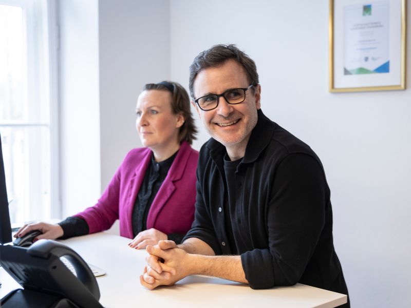 Zwei Mitarbeiter in einem modernen Büro, einer von ihnen lächelt, während der andere auf den Bildschirm schaut.