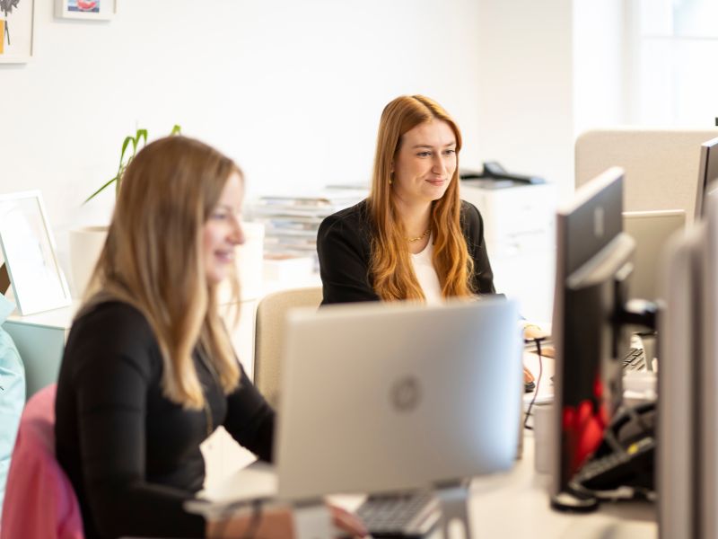 Zwei Frauen arbeiten konzentriert in einem modernen Büro an ihren Laptops, umgeben von einer inspirierenden Arbeitsumgebung.