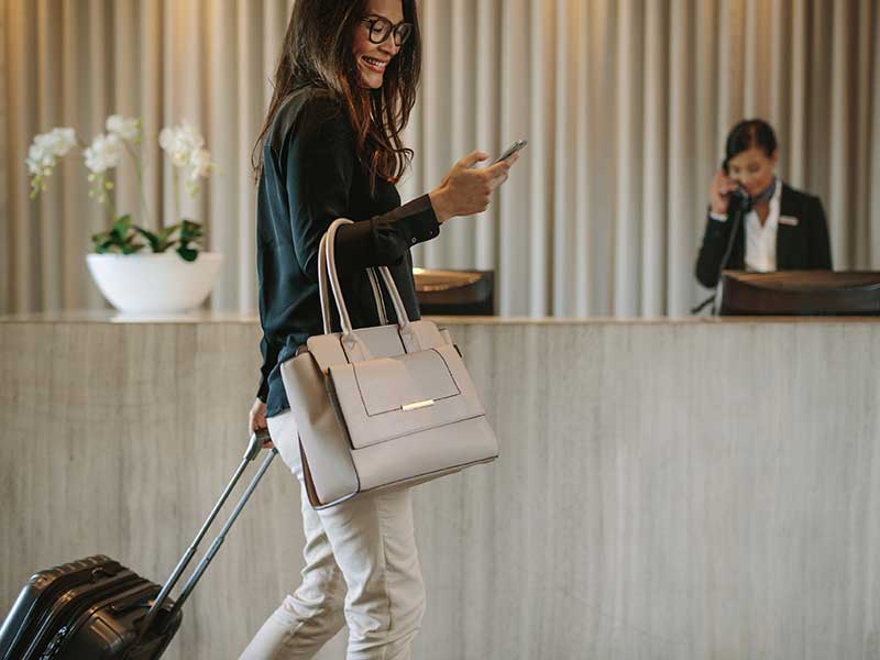 Eine Frau in der Hotellobby mit Koffer und Smartphone, bereit für den Check-in, in einem modernen Hotel.