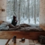 Person sitzt in einer Holzblockhütte im Schnee, genießt die Aussicht auf den winterlichen Wald beim Entspannen in der Natur.