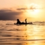 Eine Surferin liegt auf ihrem Board im Wasser bei Sonnenuntergang, ideal für Abenteuerlustige in Küstenregionen.