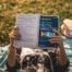 Eine Person liegt auf einer Wiese und liest das Buch „Understanding Digital Marketing“, während sie sich entspannt und eine Erfrischung daneben hat.