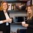Zwei lächelnde Frauen stehen im Büro und unterhalten sich bei Kaffee, umgeben von modernen Büro-Utensilien und Geräten.