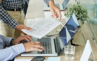 Zwei Kollegen arbeiten an einem Laptop in einem modernen Büro, analysieren Designs und besprechen Pläne während eines kreativen Meetings.