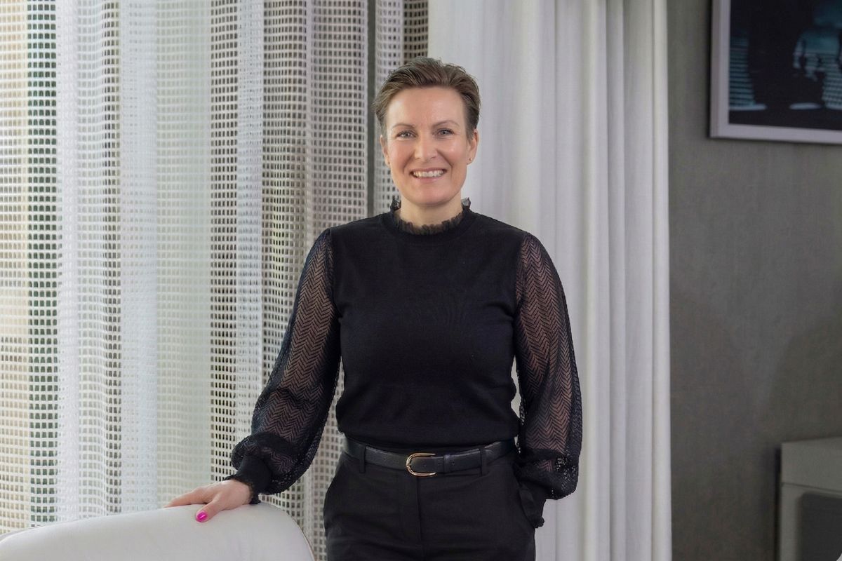 Eine stilvolle Person steht in einem modernen Raum mit eleganter Inneneinrichtung, Vorhängen und harmonischer Beleuchtung.