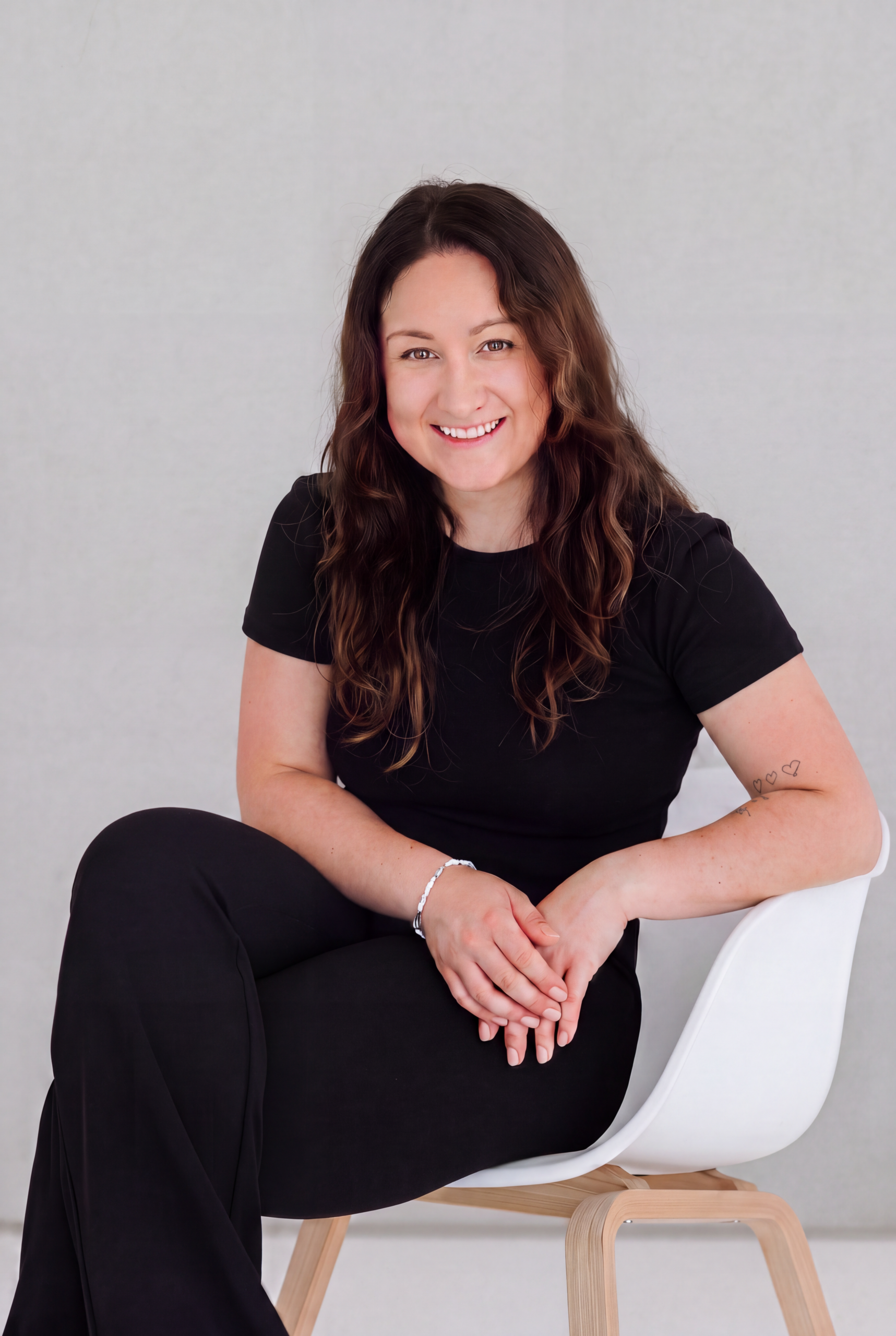 Professionelles Porträt einer lächelnden Frau in einem modernen Umfeld Porträt einer lächelnden Frau in einem Stuhl vor einem neutralen Hintergrund, ideal für Business- oder Bewerbungsfotos.